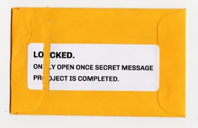 Scan of ripped open yellow packet: 'LOCKED. ONLY OPEN ONCE SECRET MESSAGE PROJECT IS COMPLETED'